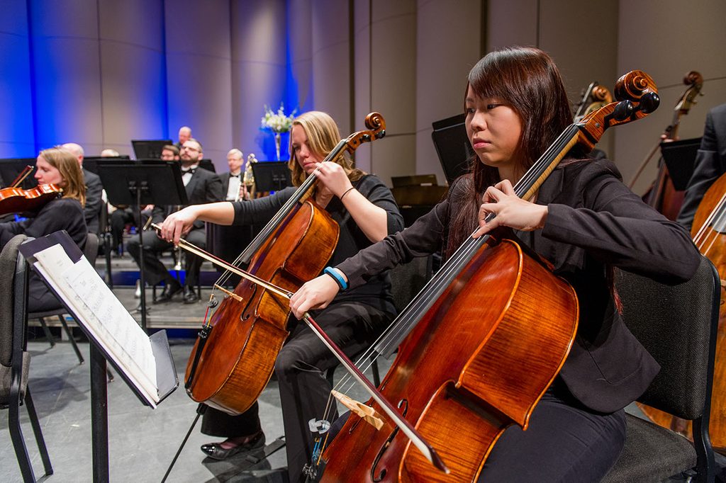 Classical musicians in a room playing cellos in front of music stands