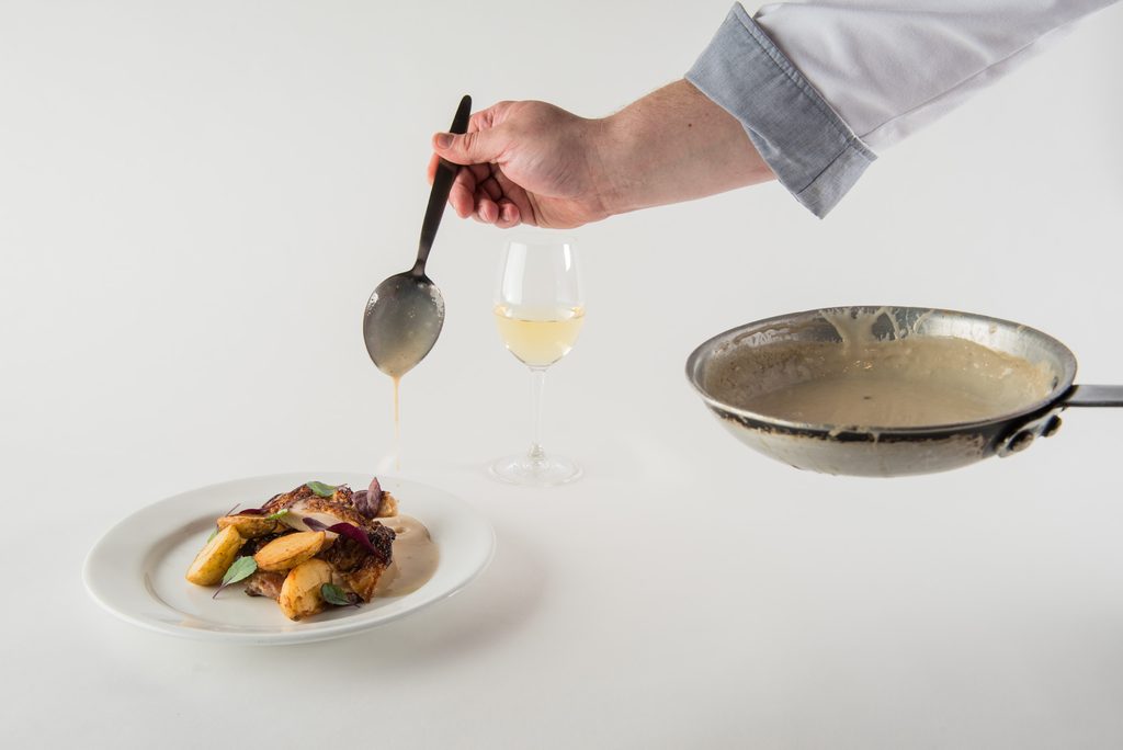 Chef's hand drizzling sauce from the pan onto a plate of food
