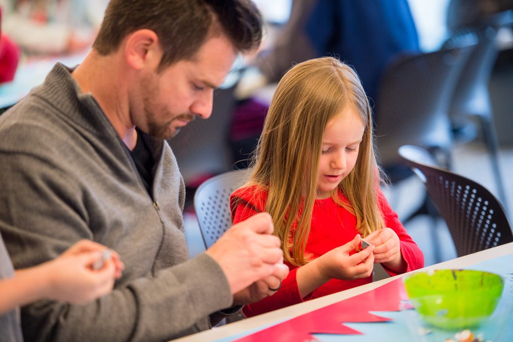 A man and girl seated at a table engaged in a craft activity with a green bowl visible.
