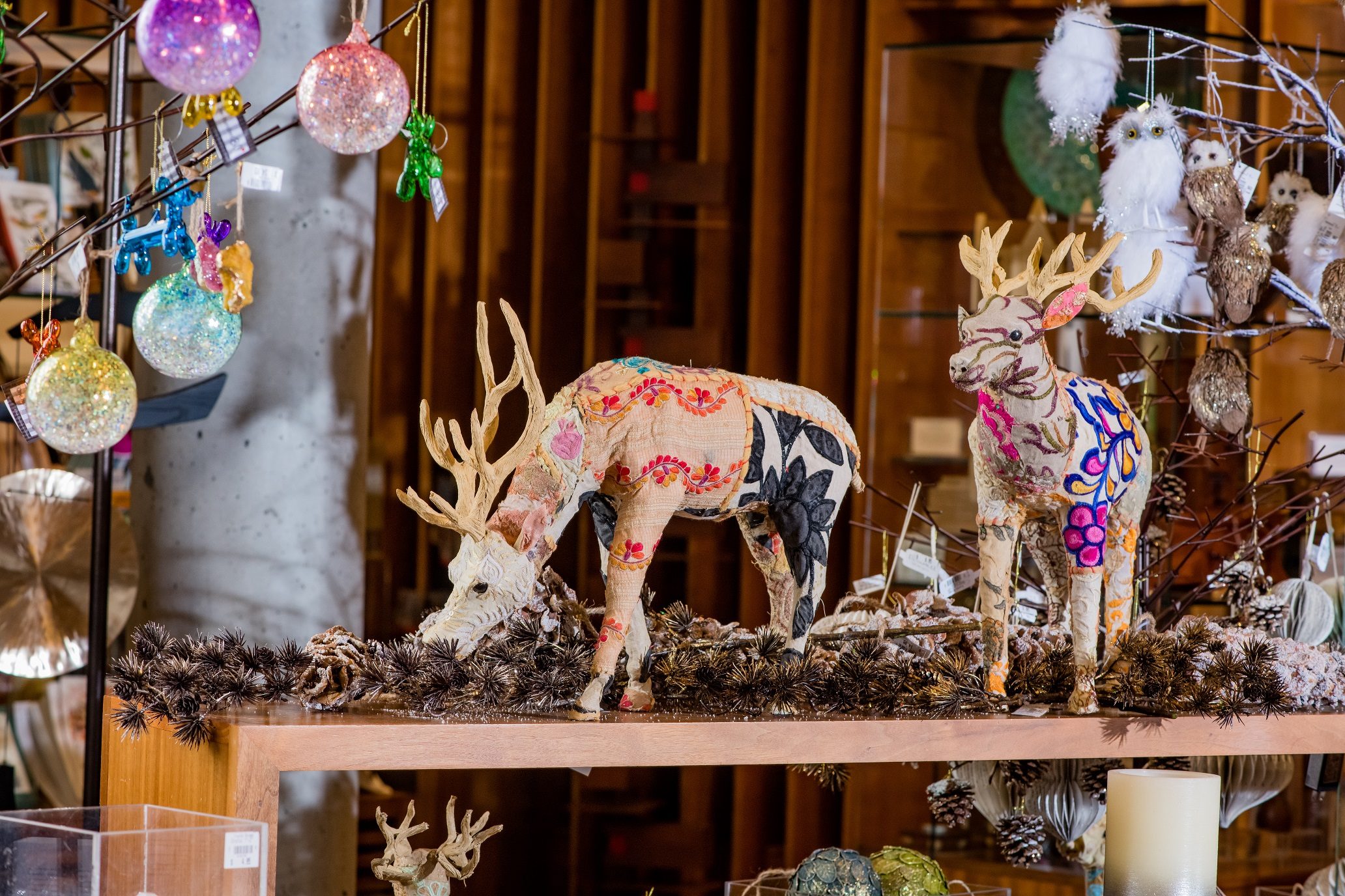 Decorative deer figures with colorful patterns on a shelf, surrounded by ornaments and pinecones.