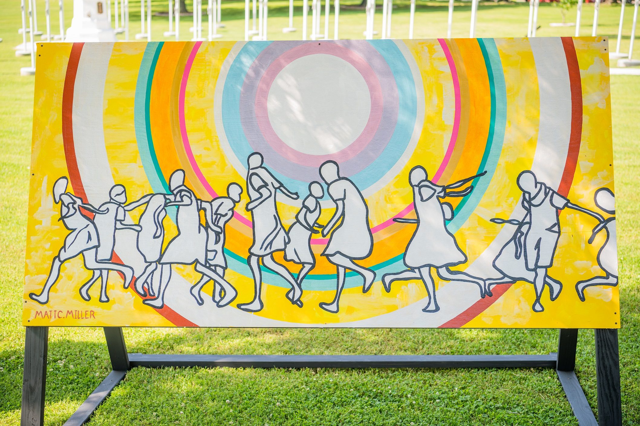 Silhouetted figures dance in front of colorful concentric circles on outdoor canvas.