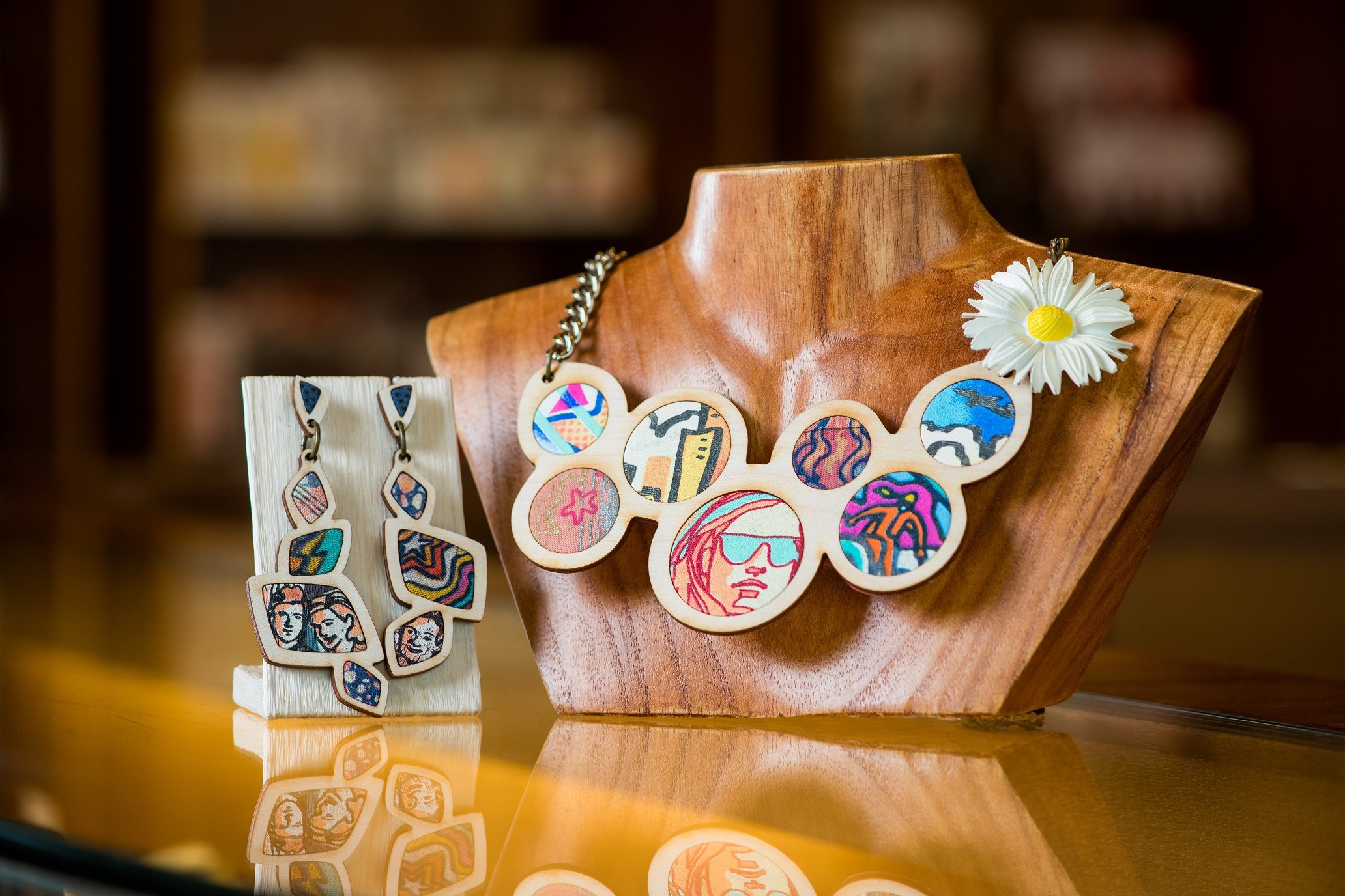 Wooden mannequin with necklace of colorful, abstract pendants and matching geometric earrings.