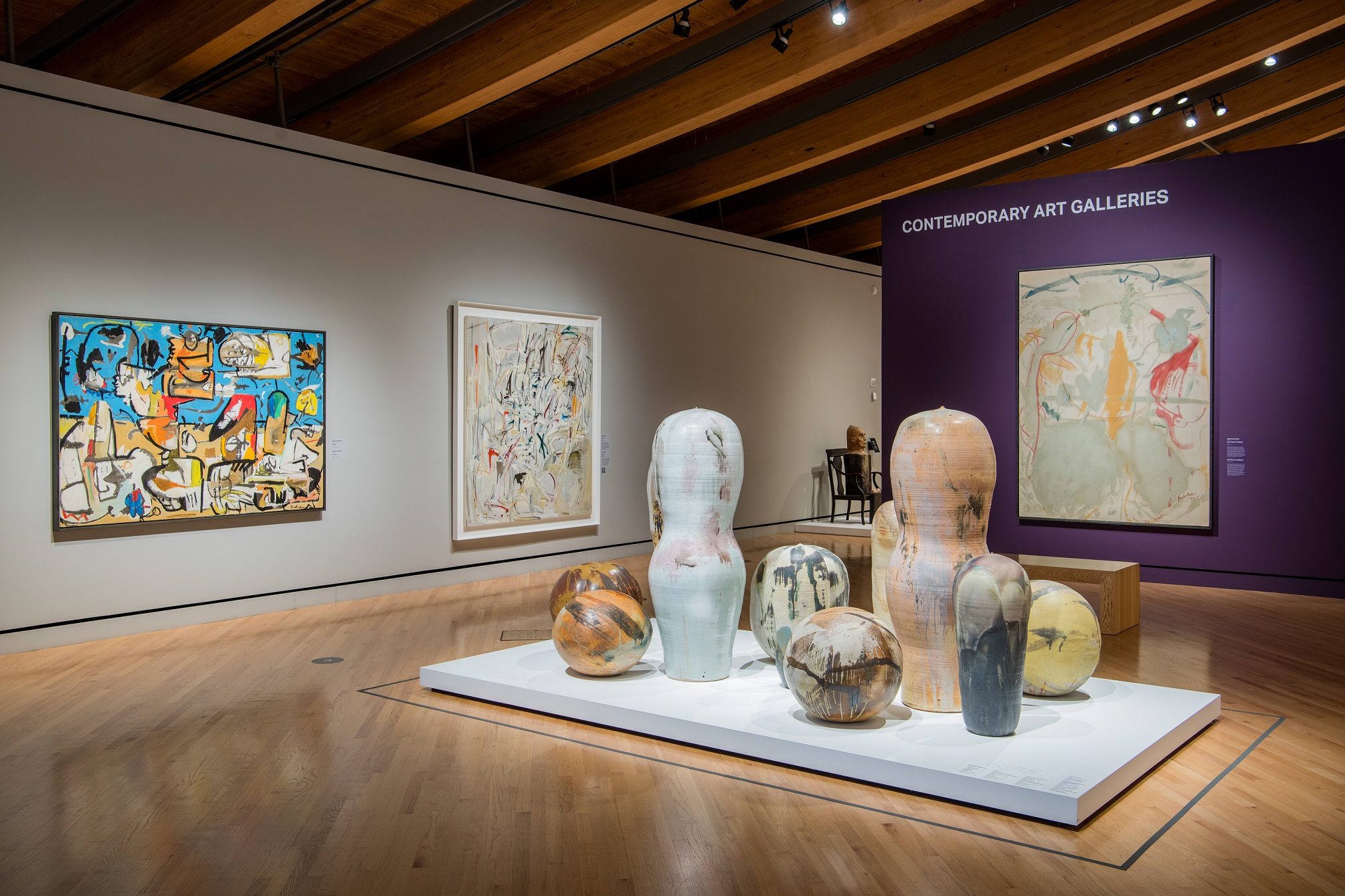 Contemporary art gallery with abstract paintings and ceramic sculptures on a wooden floor.