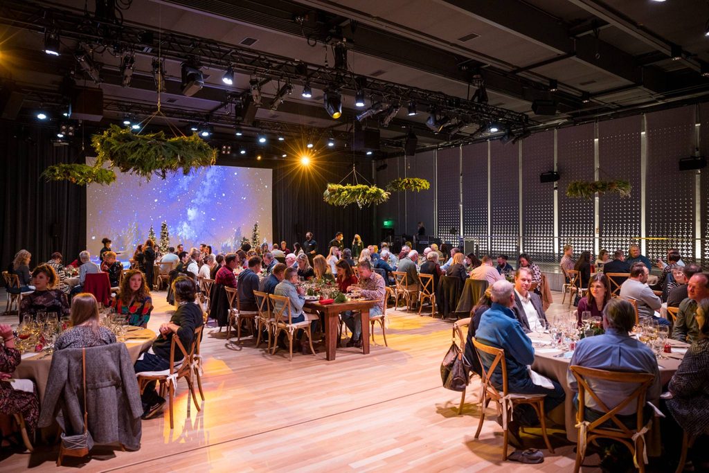 a crowd of people sitting at tables decorated for the holidays underneath wreath chandeliers
