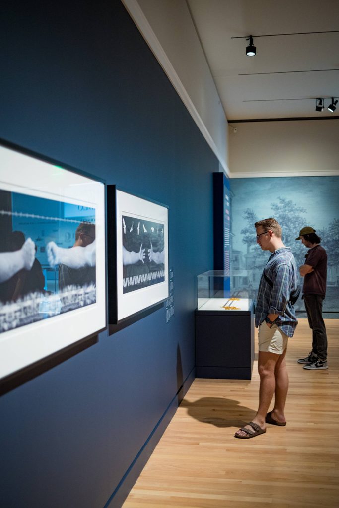 a person in a gallery stares at photograph works on a gallery wall from a side angle