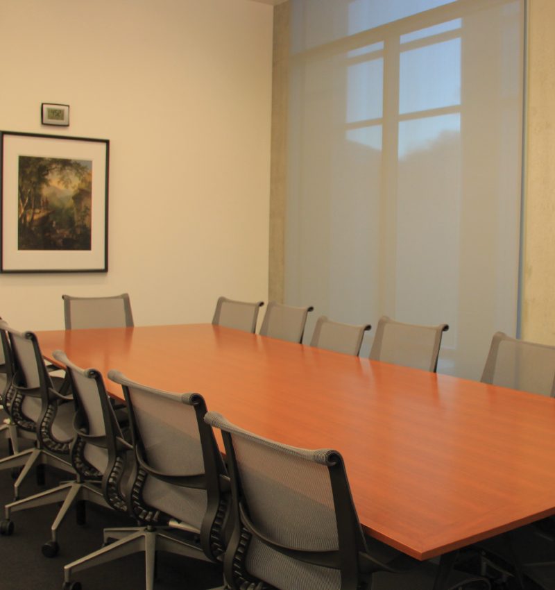 Conference room with wooden table, ten mesh chairs, large window, and framed artwork on wall.