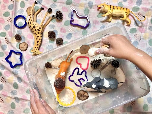 Child's hands playing with toy animals and cutters in soft material on polka dot fabric background.