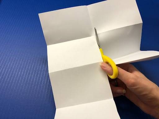 make your own sketchbook art activity; this image features a person cutting a creased piece of paper with scissors