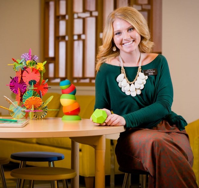 Person smiling at a table with colorful geometric shapes, sitting in a room with yellow decor.