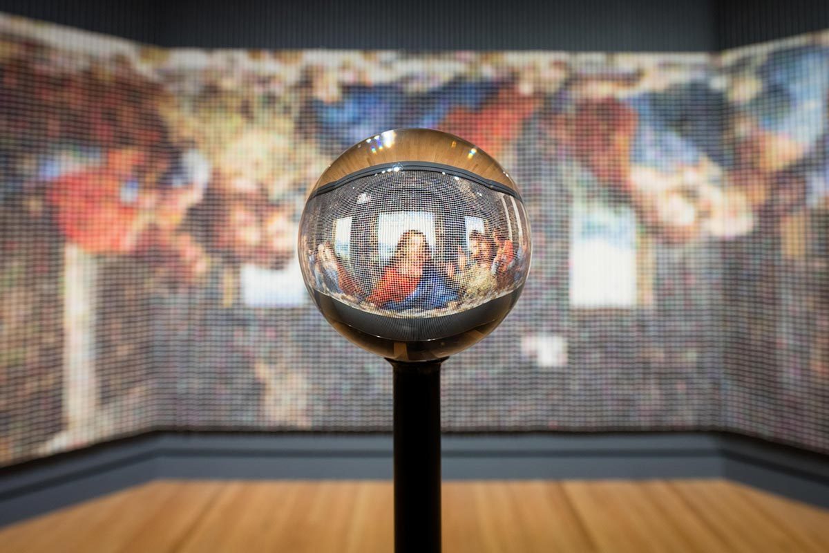 Reflective sphere distorts and magnifies pixelated mural depicting a famous artwork.