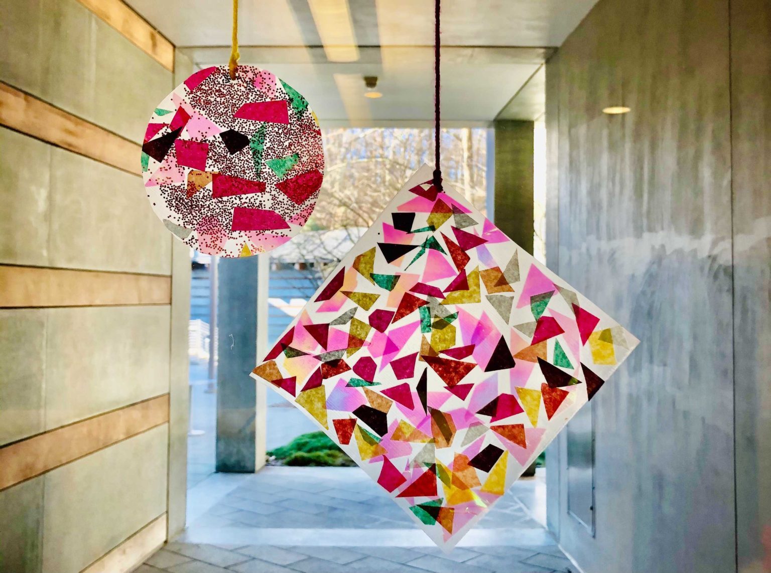 Colorful paper crafts with geometric patterns hanging indoors, one circular, one square.