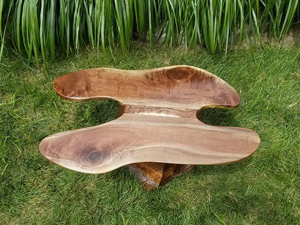 Wooden table with organic shape on grass, featuring polished finish and natural wood grain.
