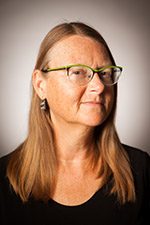 Person with long hair and glasses, facing slightly sideways against a neutral background.