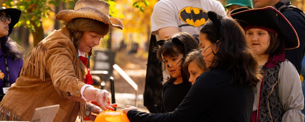 Children and adults in Halloween costumes outdoors receiving treats in pumpkin buckets.