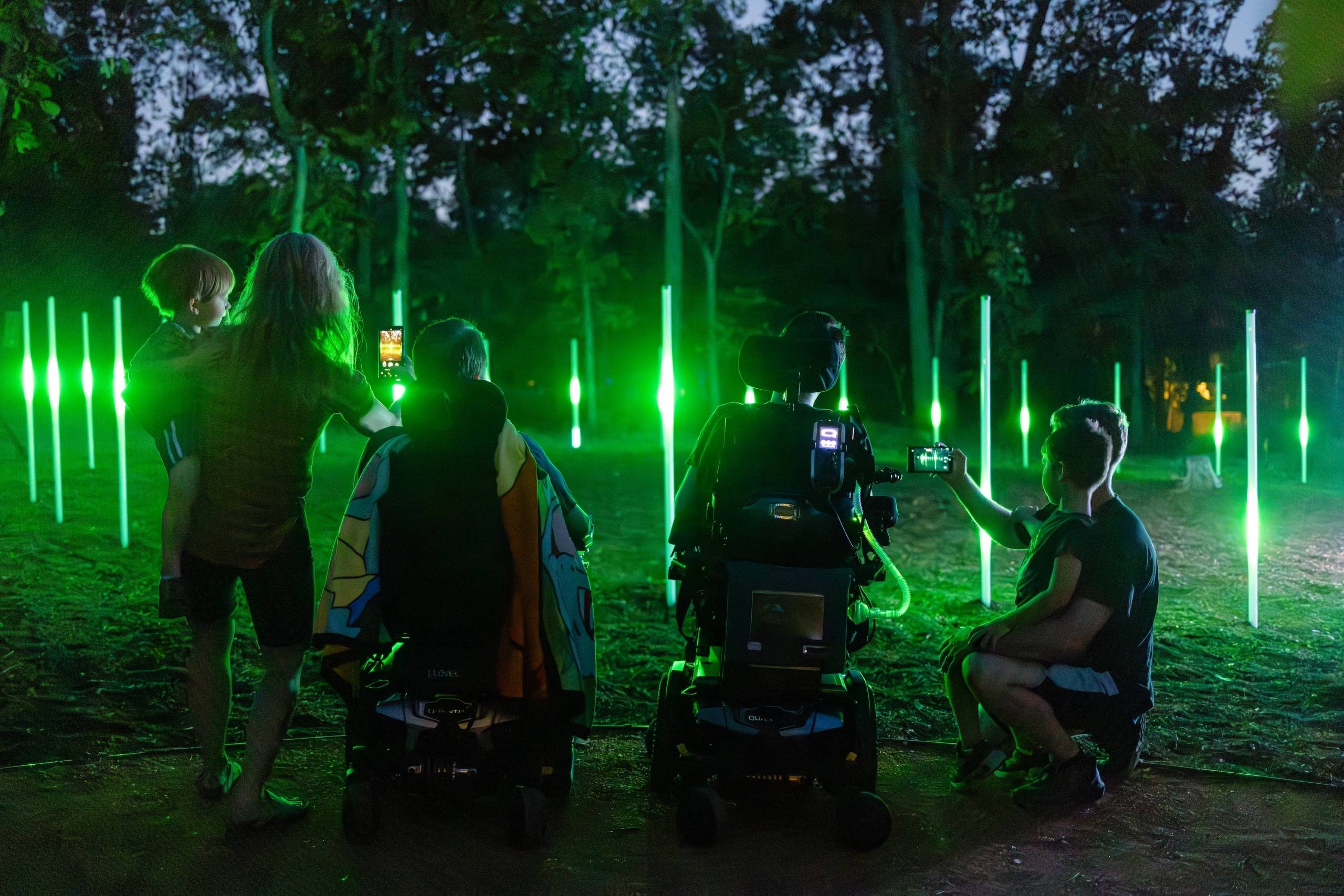 Two guests in wheelchairs and two guests kneeling in front of a light installation in the North Forest