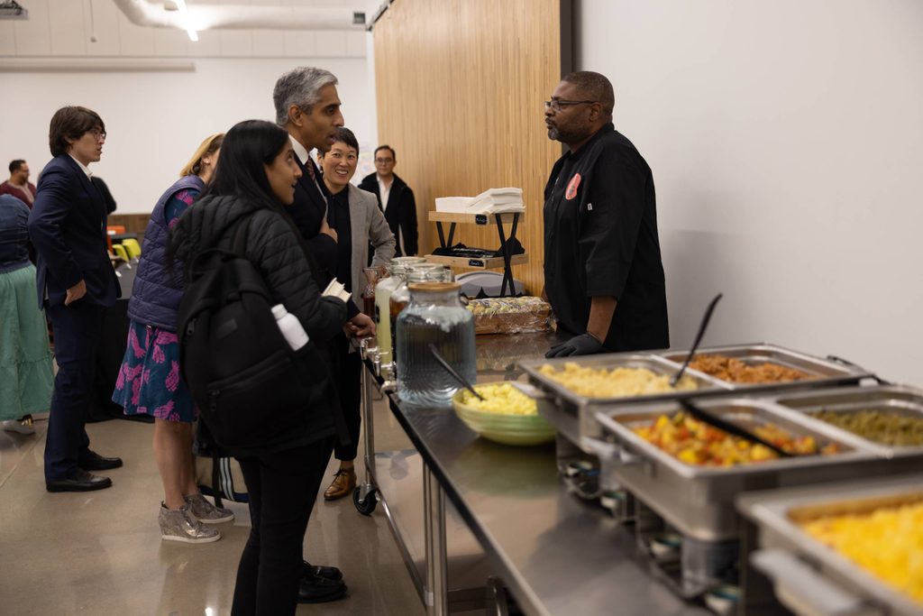 People at a food station with a chef indoors, dishes and beverages on display