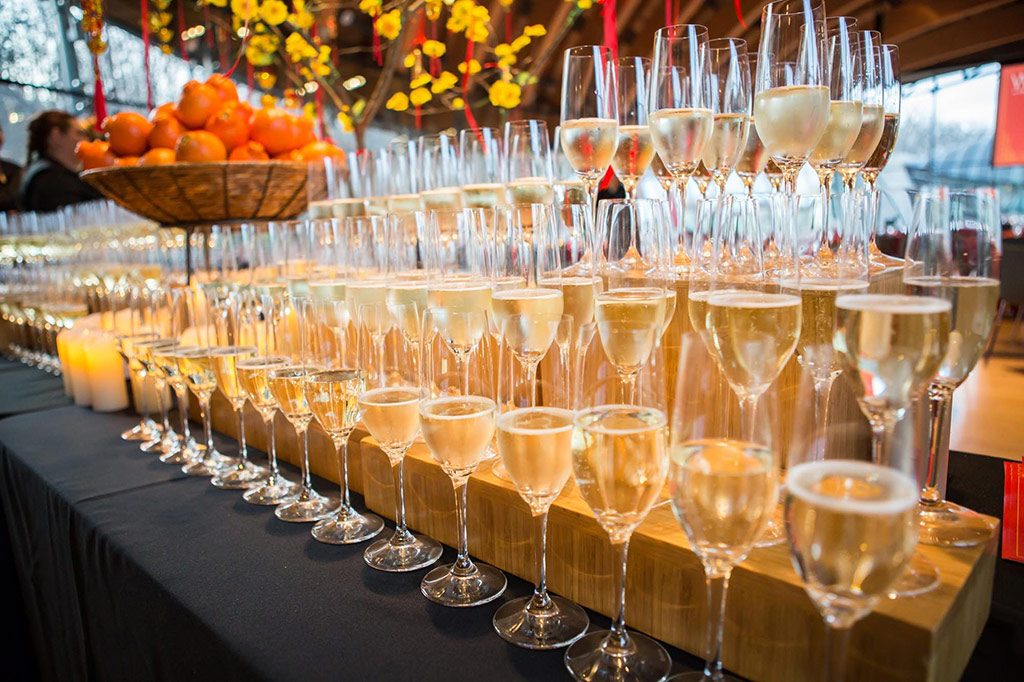 Rows of wine glasses on a wooden display stand, sitting on a black table cloth next to a floral arrangement
