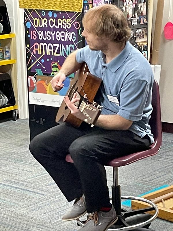 a man sits in a chair in a classroom playing guitar