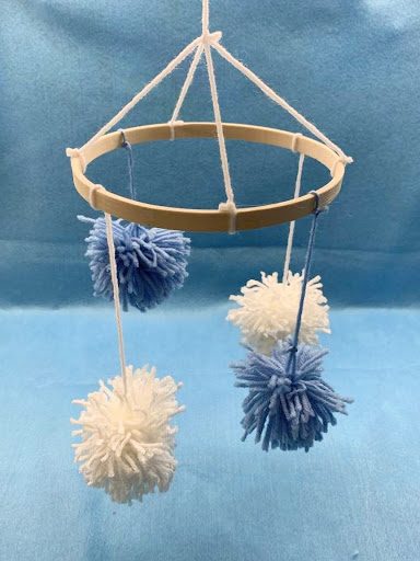 blue and white pom poms hanging from a circular wooden frame against a blue backdrop