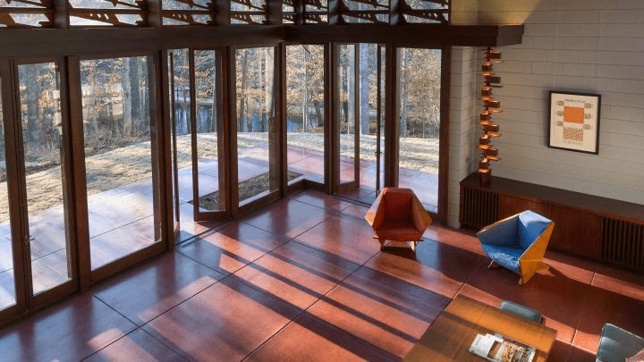 Modern room with glass doors, polished floor, red and blue chairs, table, and framed artwork.