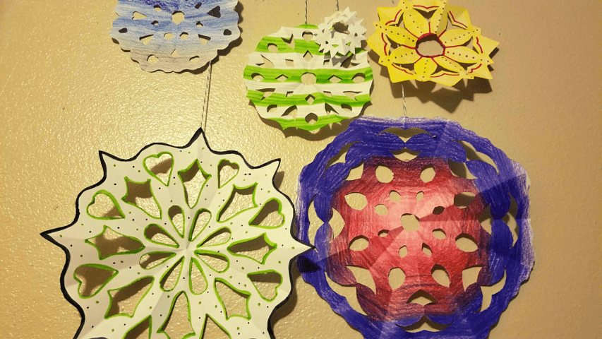 Colorful paper snowflakes with intricate patterns hang against a wall.